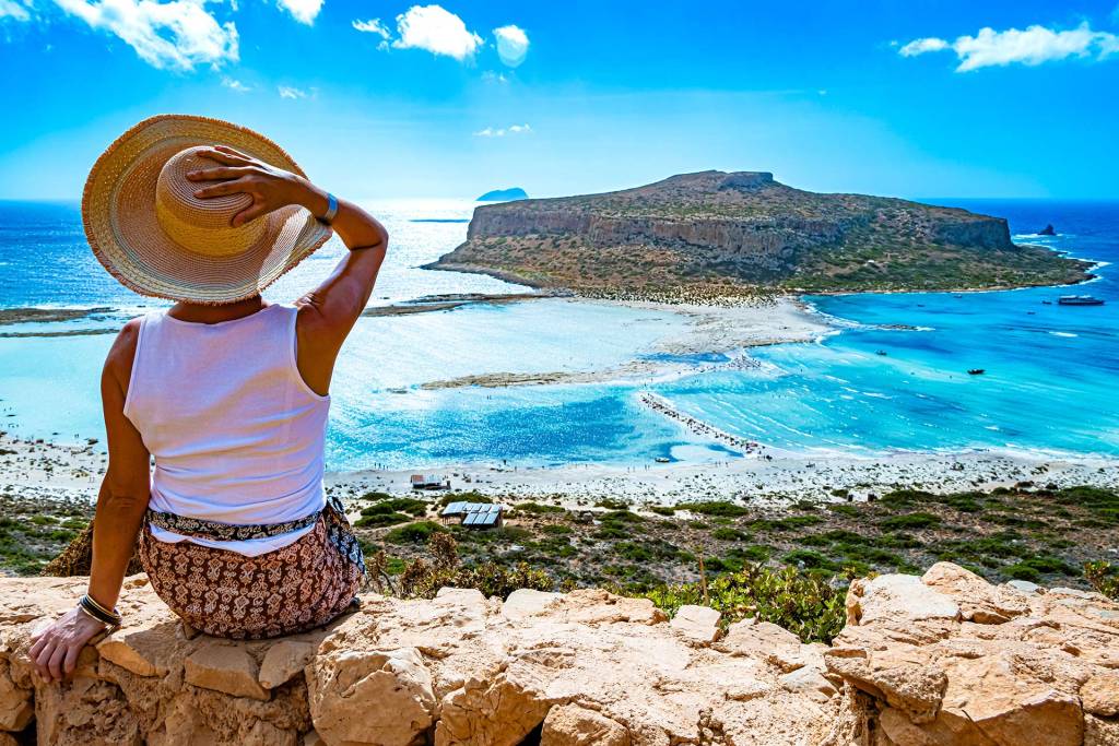 A woman holds her hat as she admires the view of Balos Beach.