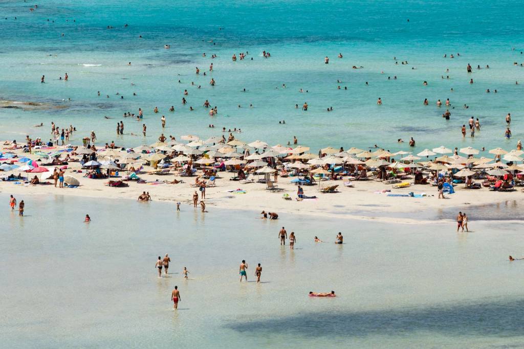 People swim and sit under umbrellas in Balos Beach.