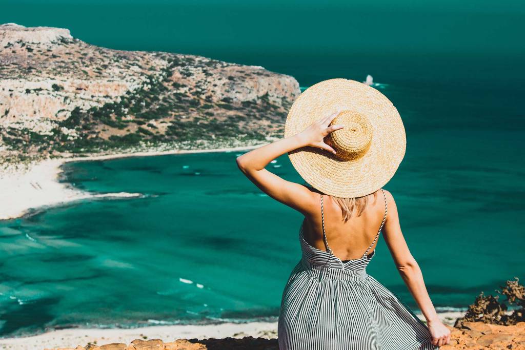 A woman wearing a hat enjoying at the sea view during her holidays in Chania.
