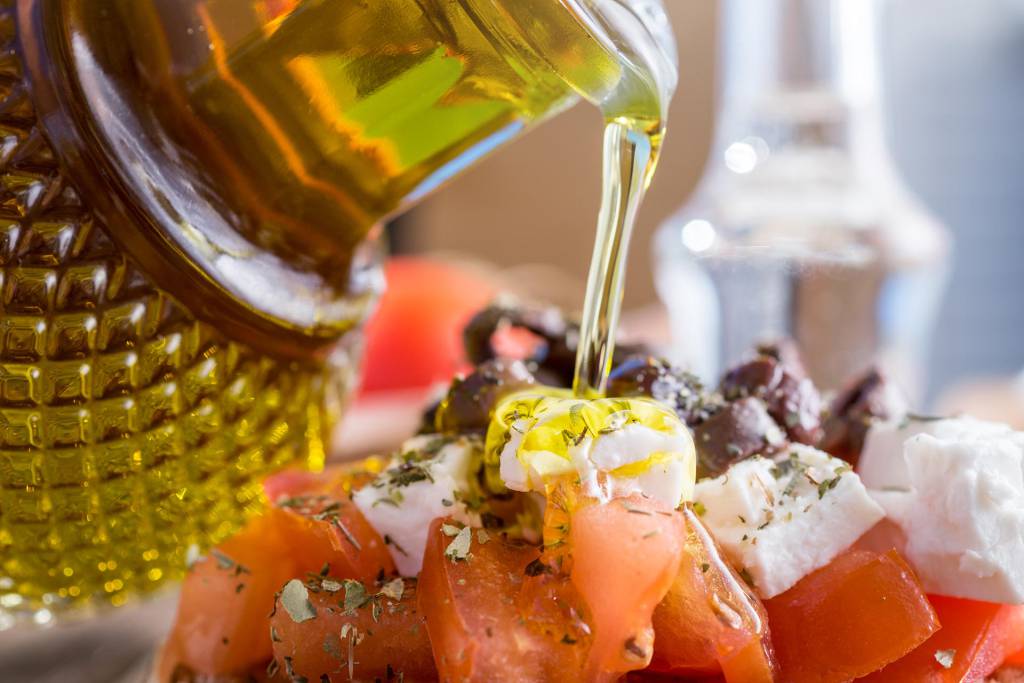 Pouring olive oil in a Cretan Dakos Salad, while having raki next to you.
