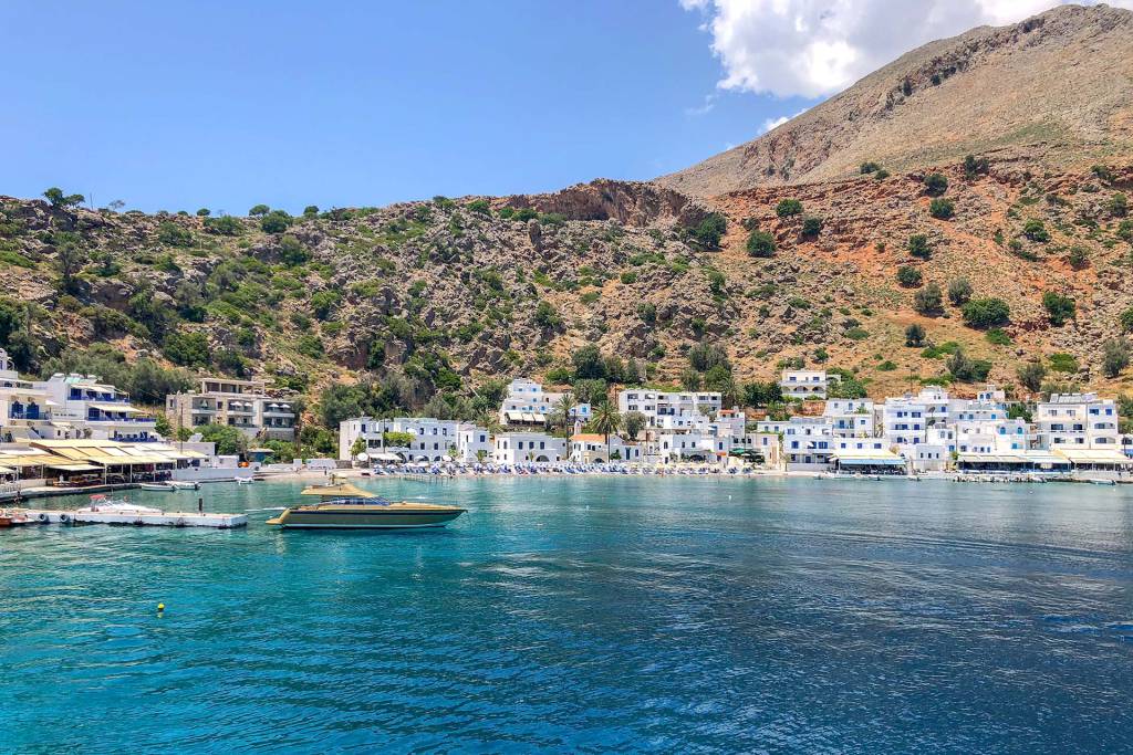 A luxurious yacht leaves the picturesque Loutro Village in South Chania, while viewing Loutro Beach and the white-washed little houses.