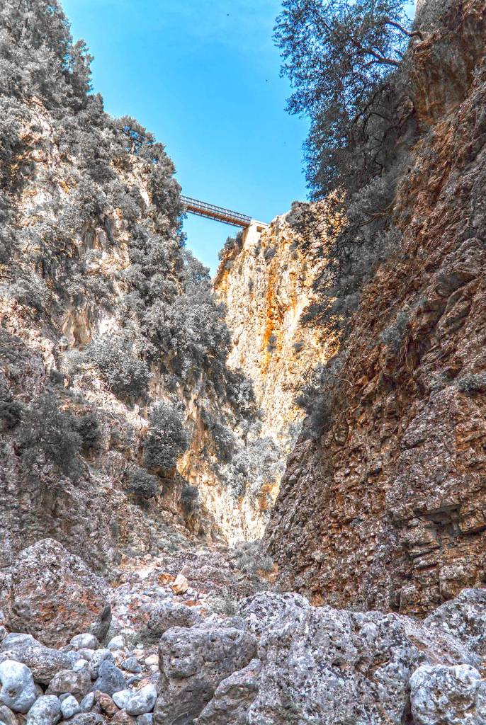 The rocky path of Aradena Gorge below a metal bridge.