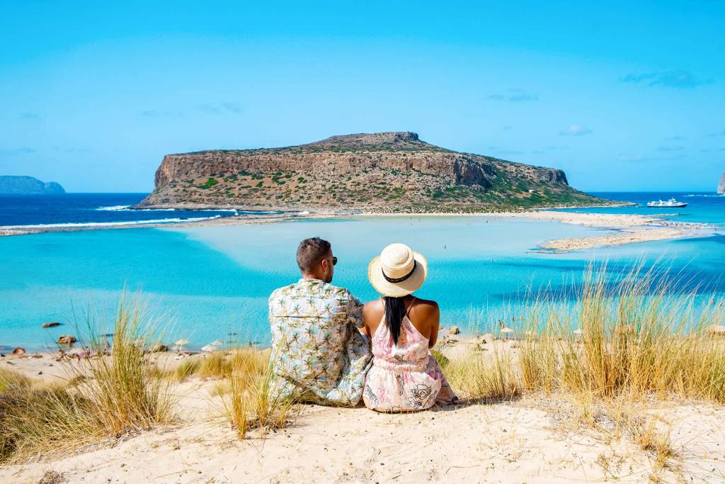 A couple sitting on a road admiring the Balos Lagoon in Chania.