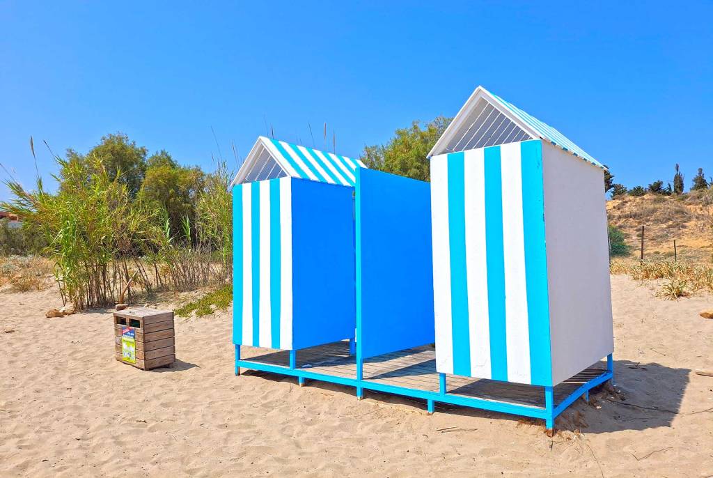 Two changing rooms next to some trees in the sandy Chrissi Akti Beach of Chania.