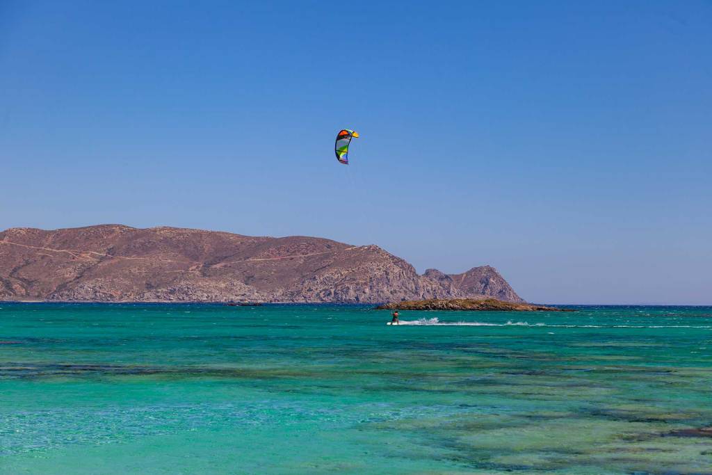 A man kitesurfing on the turquoise waters of Elafonisi Beach.