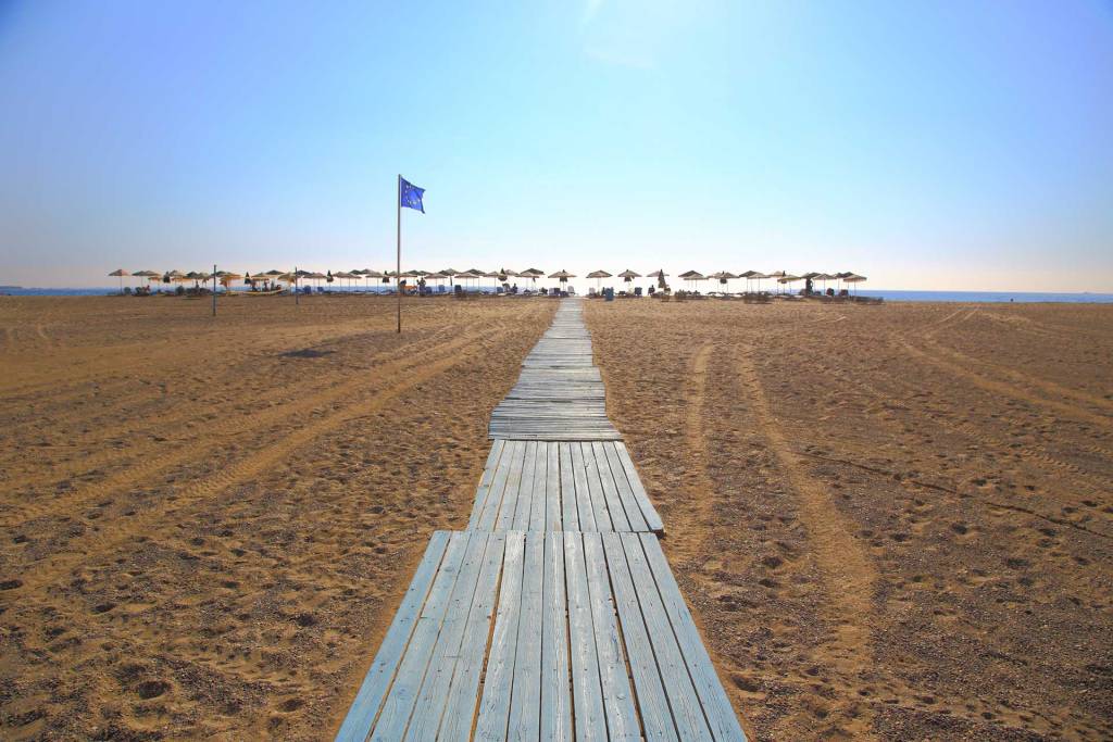 The EU flag, the sandy coast, and umbrellas in Falassarna Beach.