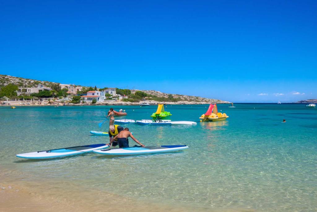 Two people on SUP boards and watersport rentals in Marathi Beach.