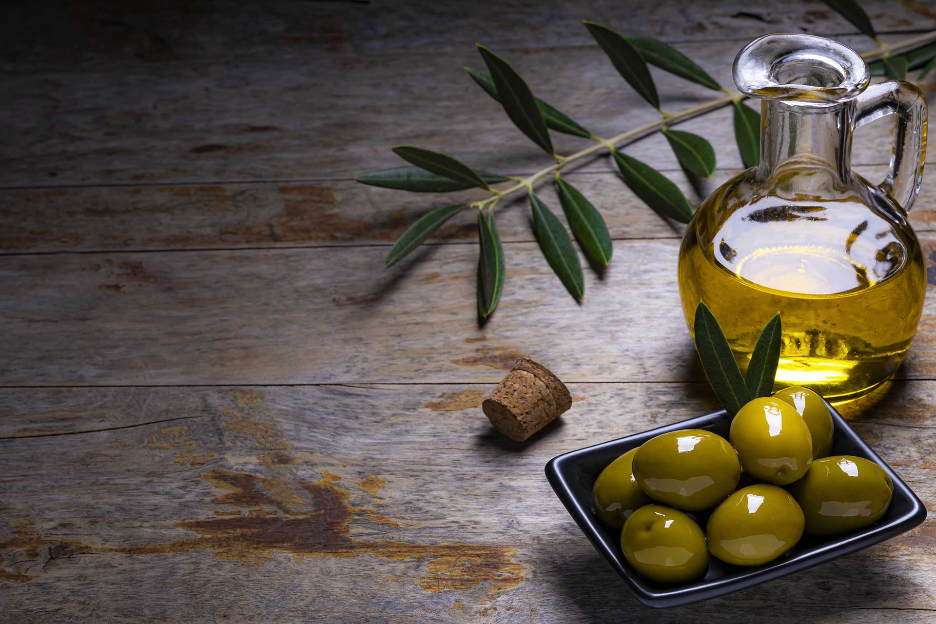 A bottle of extra virgin olive oil and a plate with green olives.
