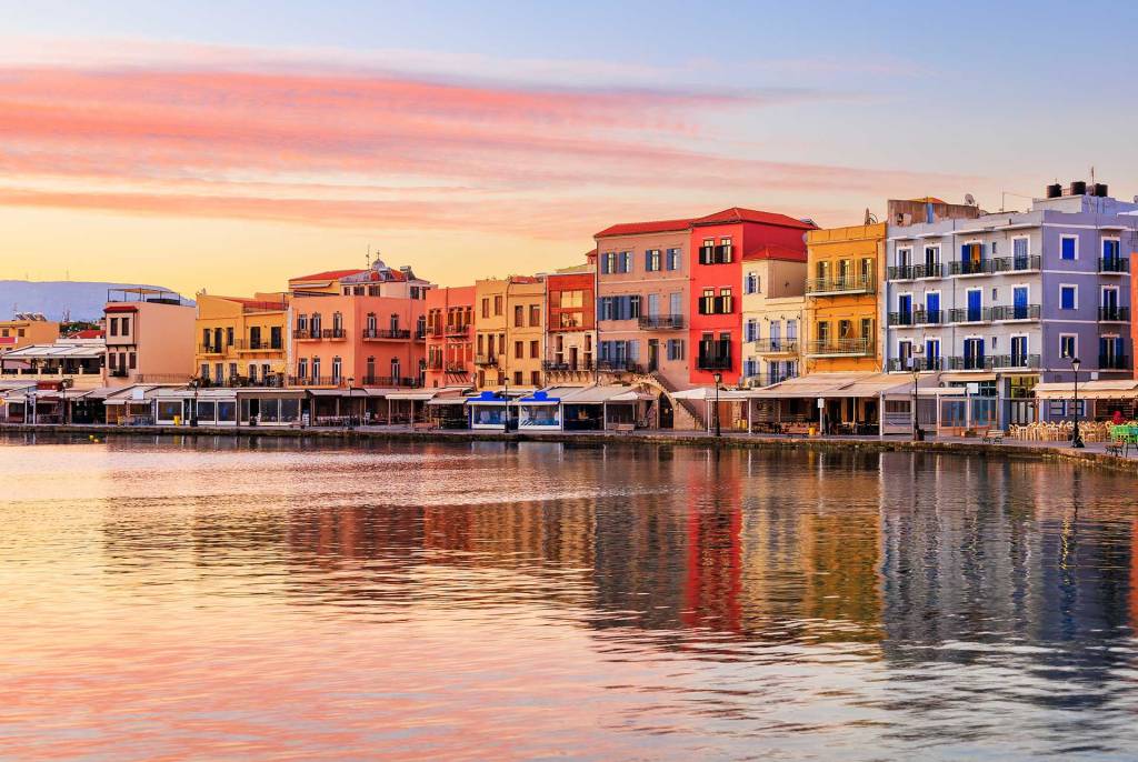 Picturesque colorful hotels in Chania Venetian Harbor, right next to the sea, during sunset.