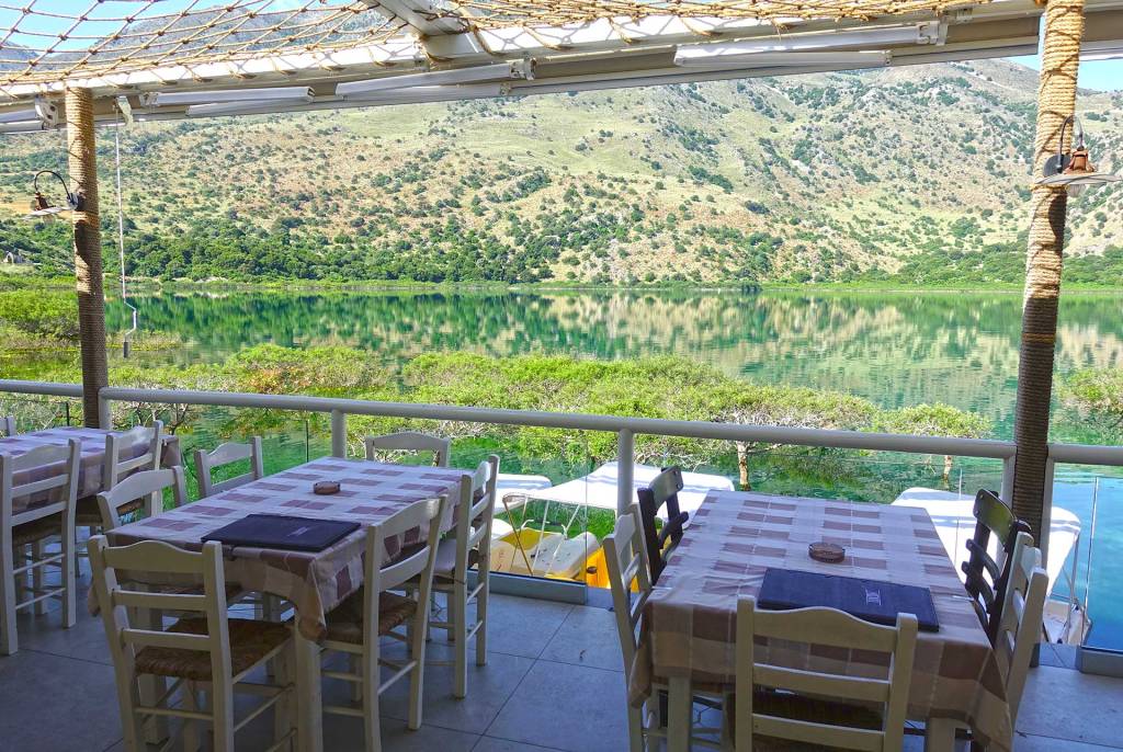 The tables and chairs of a small restaurant in Lake Kournas offering magnificent views of the lake and the mountain.