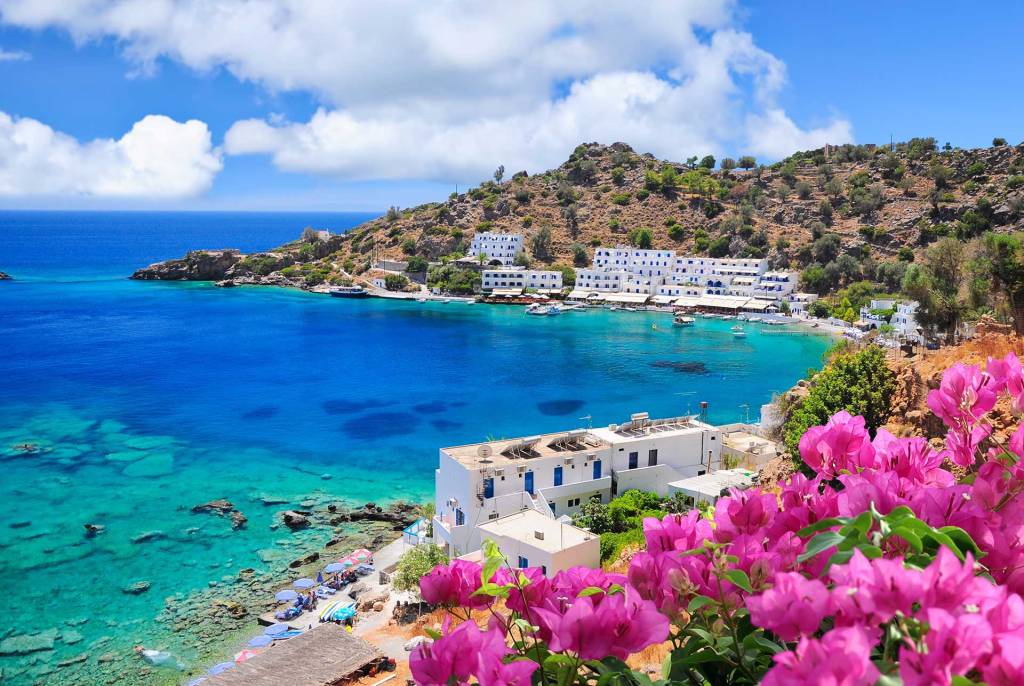 White-washed houses, hotels, and pink flowers next to the sea of the picturesque Loutro Village in South Chania.