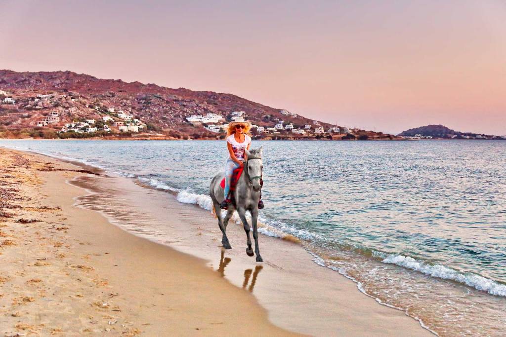 A woman enjoys a horseback riding experience on a sandy beach in Naxos.