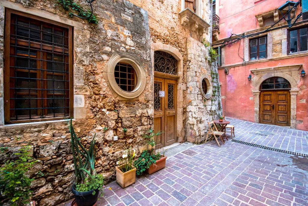 A picturesque stone-built hotel with flowers and a wooden door in the heart of Chania Old Town.
