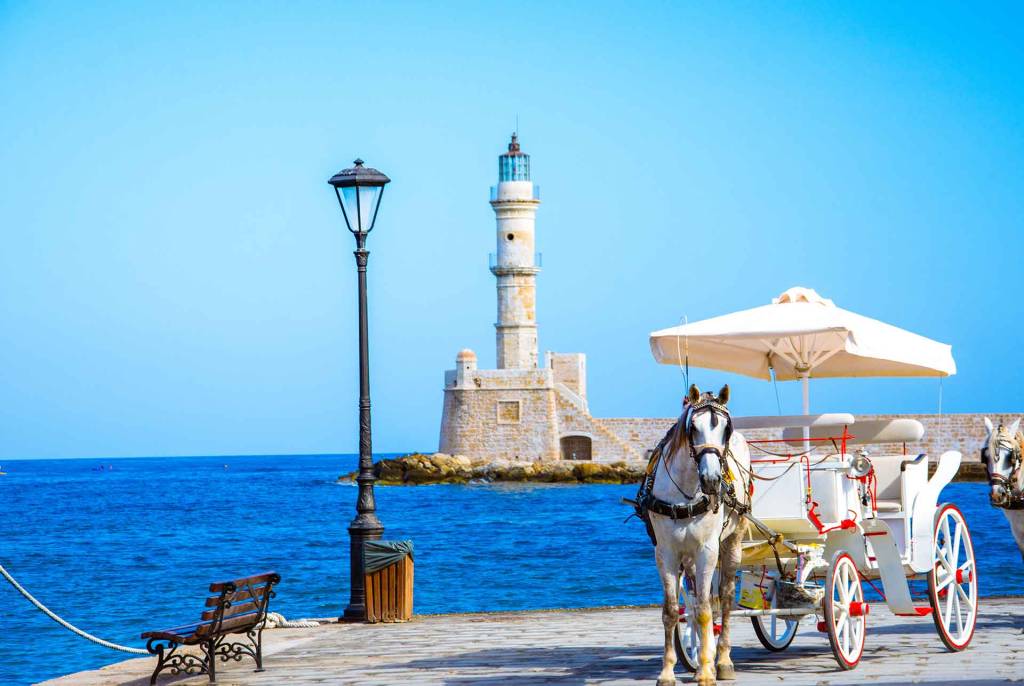 A horse carriage with the background view of the lighthouse of Chania.