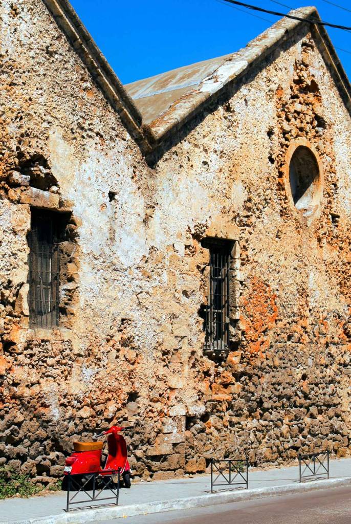 A red motorbike next to the stone-built Venetian Shipyards (Neoria), an epitome of architecture in Chania.