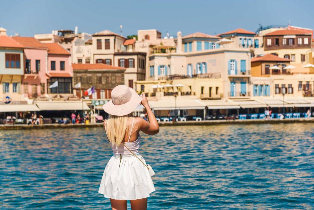 A young tourist is taking photos of the picturesque buildings in Chania Venetian Harbor.