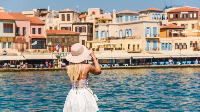 A young tourist is taking photos of the picturesque buildings in Chania Venetian Harbor.