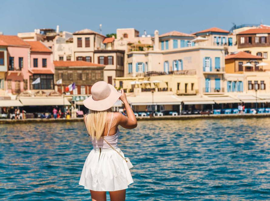 A young tourist is taking photos of the picturesque buildings in Chania Venetian Harbor.