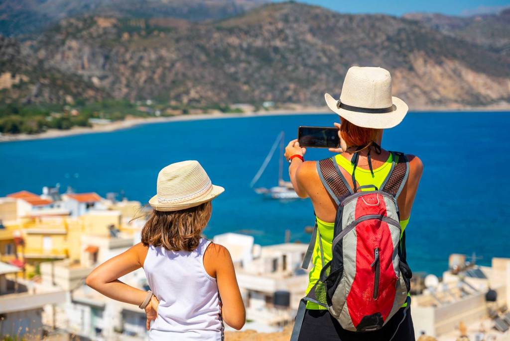 A kid next to its mother who takes a photo of Paleochora Beach.