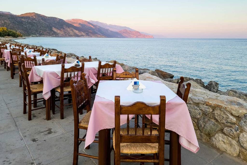 Chairs and tables of a small seaside restaurant in Paleochora Town (South Chania), right next to the sea, providing also mountain views.