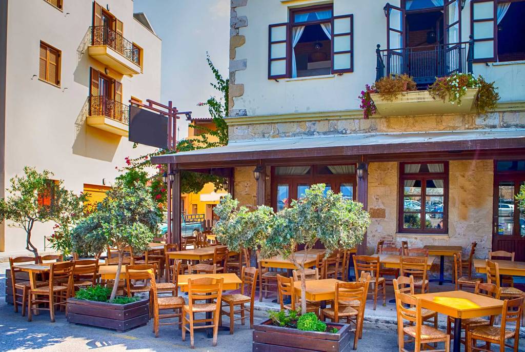 The exterior wooden chairs, tables, and trees of the awarded Chrisostomos Restaurant in Chania Old Harbor.