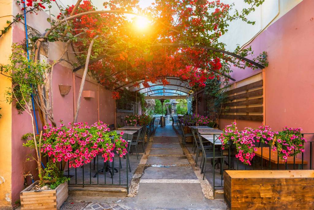 The sunset view of a restaurant with flowers, chairs, and tables in Daliani Street, close to Chania Old Town.