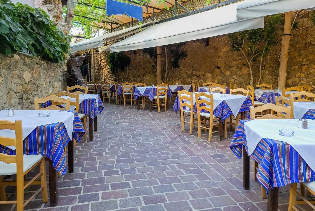 The wooden chairs and tables of a picturesque, little restaurant in Chania Old Town, on the paved sidewalk.