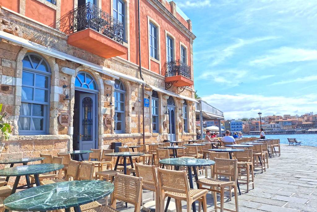The stone building and the elegant tables of the Pallas Bar Restaurant in the heart of Chania Old Harbor, offering sea views.