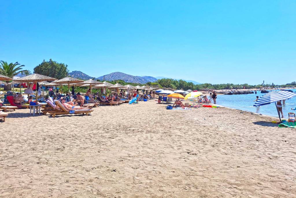 The sandy Grammeno Beach with tourists sitting at their sunbeds.
