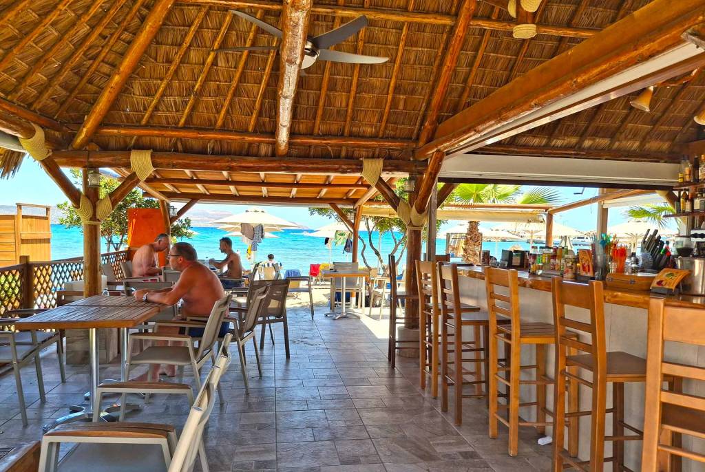 The wooden chairs, tables, and ceiling of a seaside beach bar in Kalyves Village.