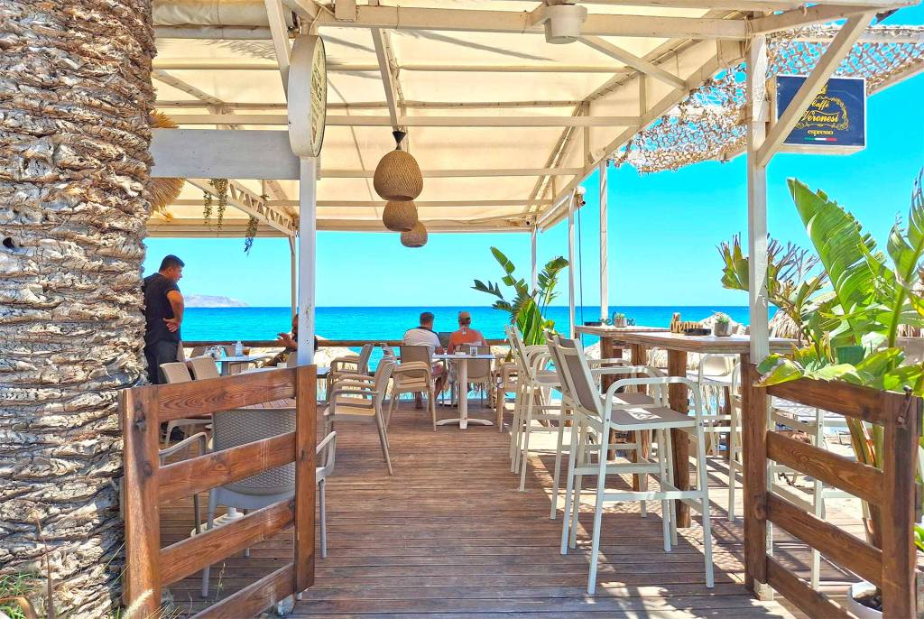 Tourists sitting at the tables of a seaside beach bar in Kalyves Village.