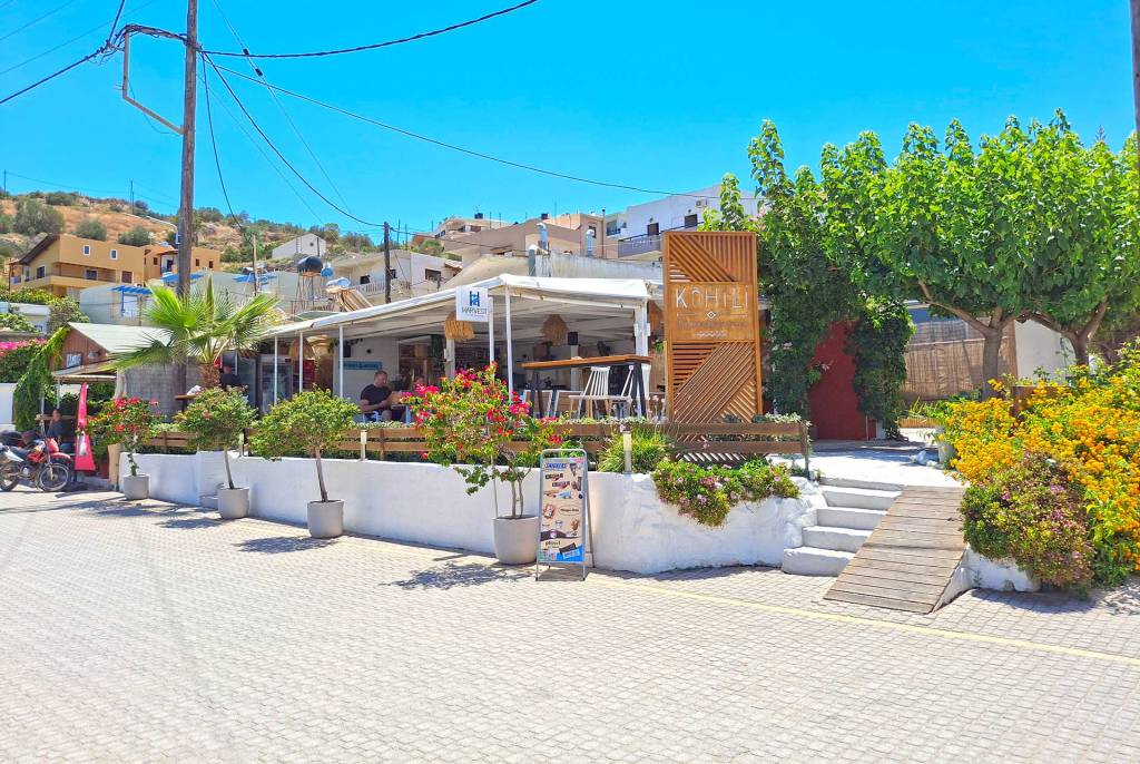 The exterior view of Kohili Beach Bar in Kalyves Village, surrounded by trees.