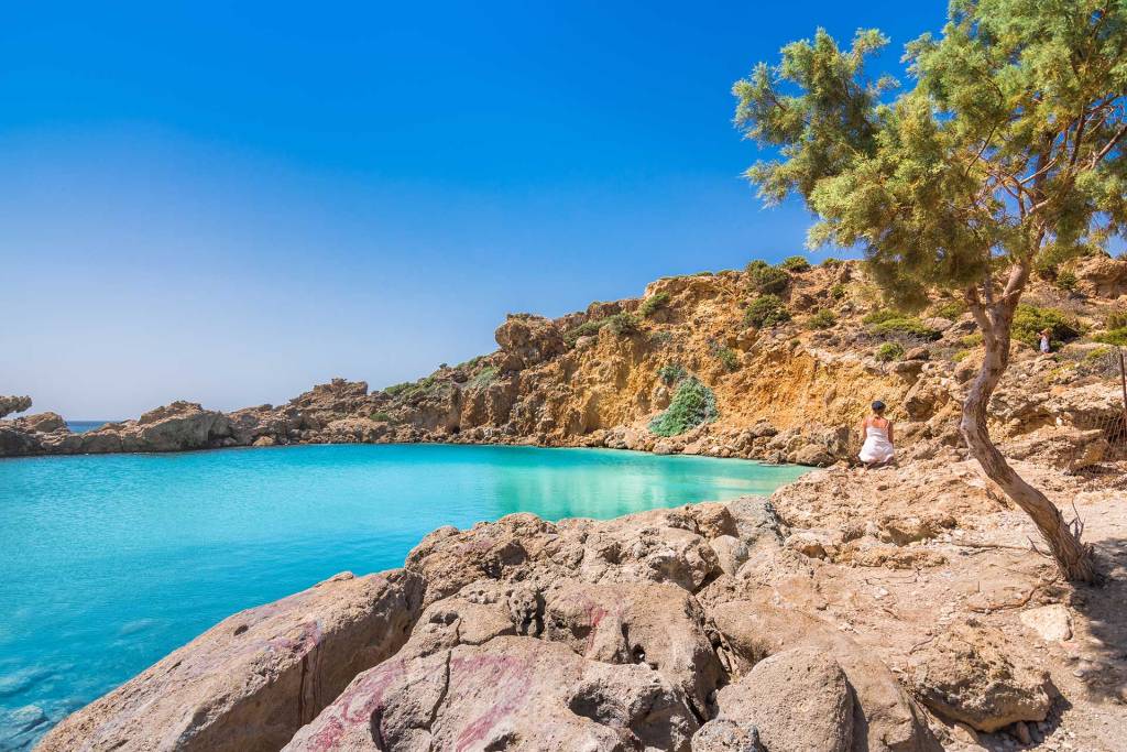 A woman sits on a rock next to Voulolimni.