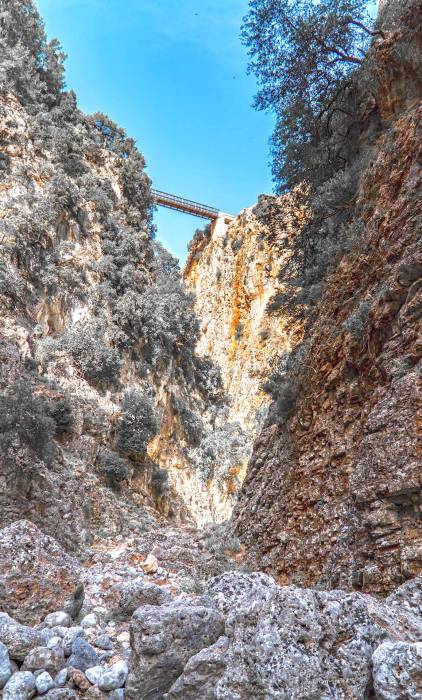 The rocky path of Aradena Gorge below a metal bridge.