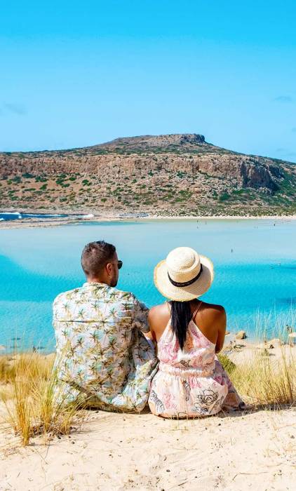 A couple sitting on a road admiring the Balos Lagoon in Chania.