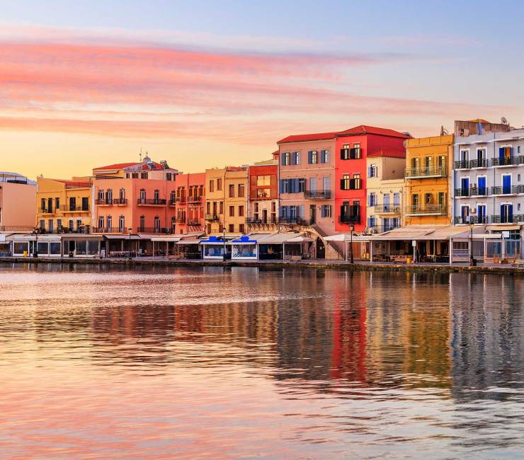 Picturesque colorful hotels in Chania Venetian Harbor, right next to the sea, during sunset.