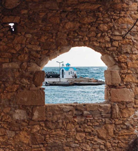 Viewing a small seaside chapel in Galatas through a stone hole.