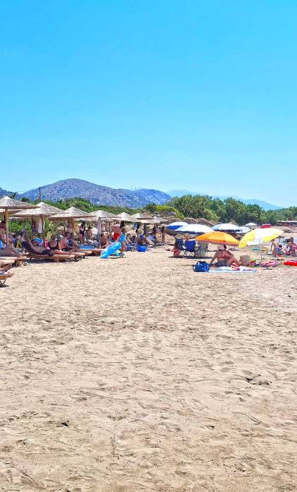 The sandy Grammeno Beach with tourists sitting at their sunbeds.