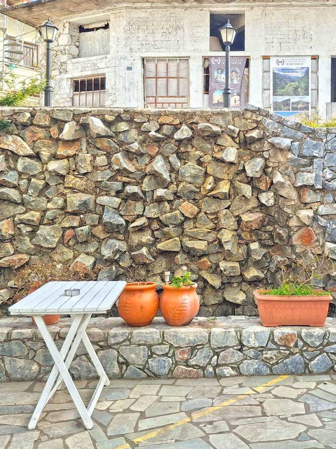 A stone wall and a white table in the square of Kandanos Village.
