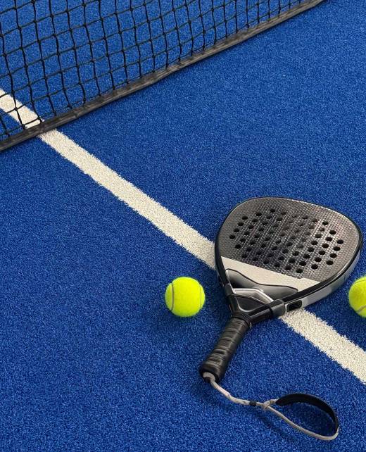 A racket and two yellow balls on the floor of a padel court.