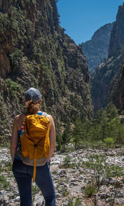 A woman wearing a backpack gazes at the landscape of Samaria Gorge.