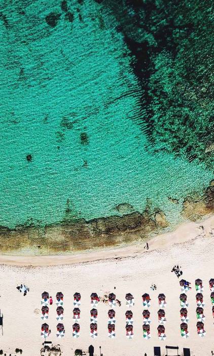 Aerial view of the turquoise waters, sandy coast, and sunbeds in Stavros Beach.