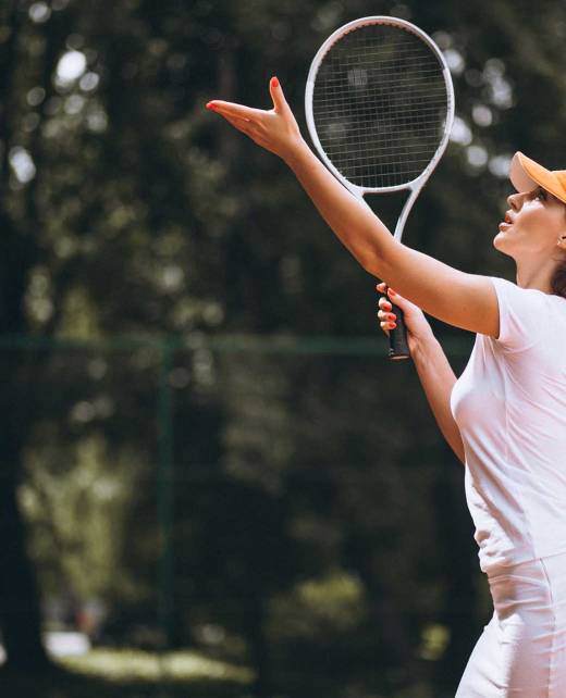 A woman plays tennis while holding her racket and wearing a hat.