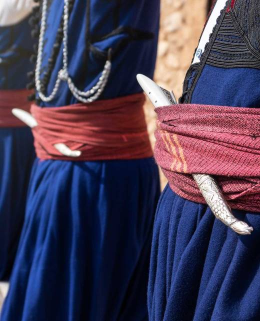 Four men dressed in Cretan Folk Costumes and wearing Cretan Knives in their belts, ready to start dancing.